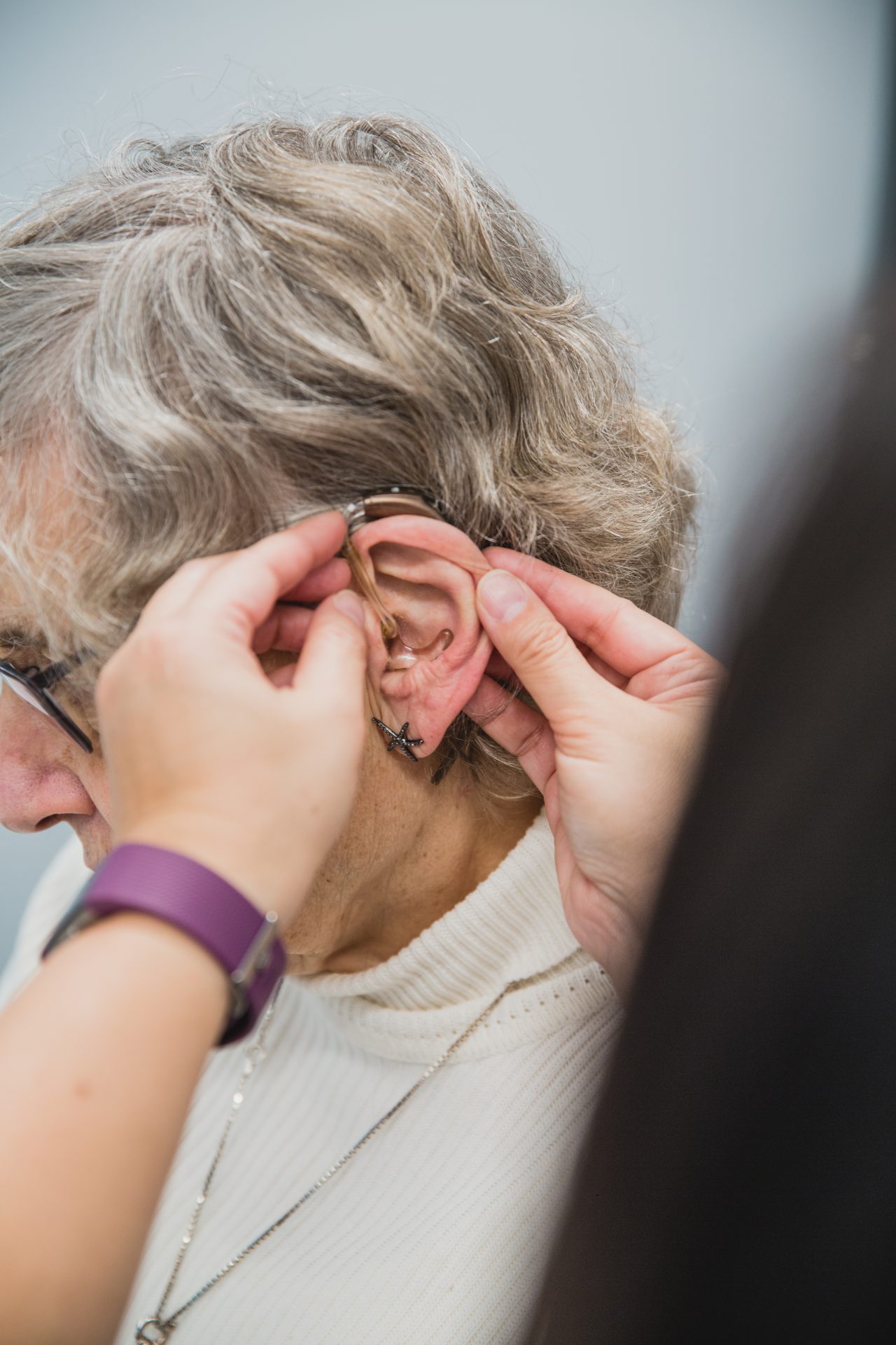 Woman has hearing aid placed on ear.