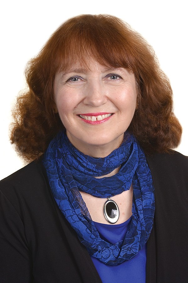 A headshot of a white woman with brown hair smiling and wearing a blue scarf and a black blouse.