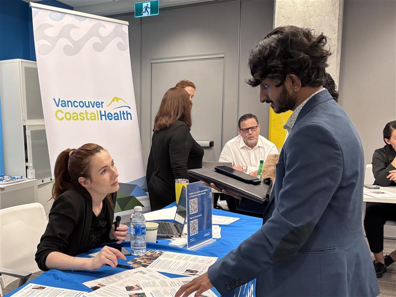 A Vancouver Coastal Health representative speaks with an attendee at an information table during a job fair.