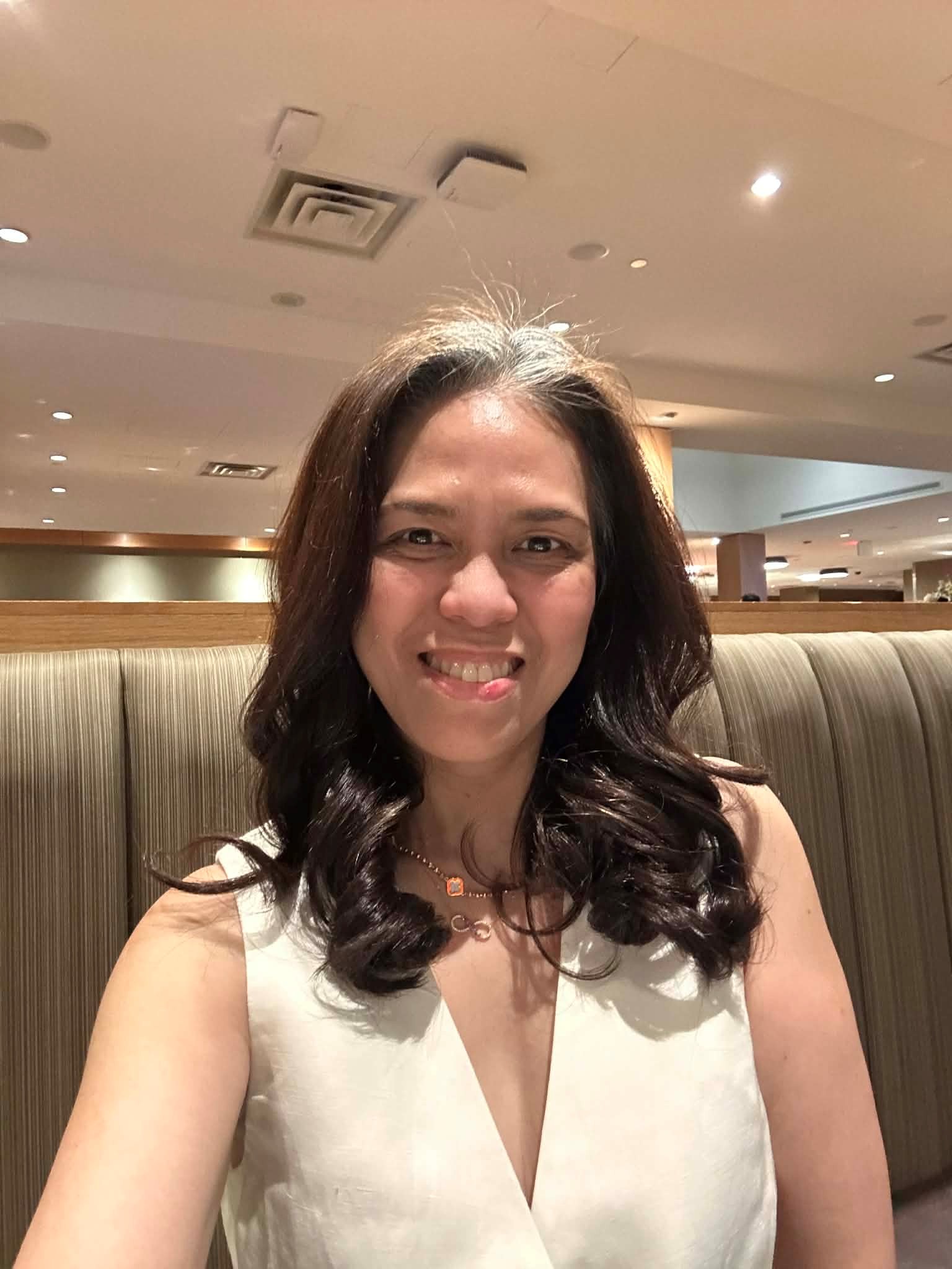 Mary Ann De Castro smiling for a selfie while seated in a restaurant.