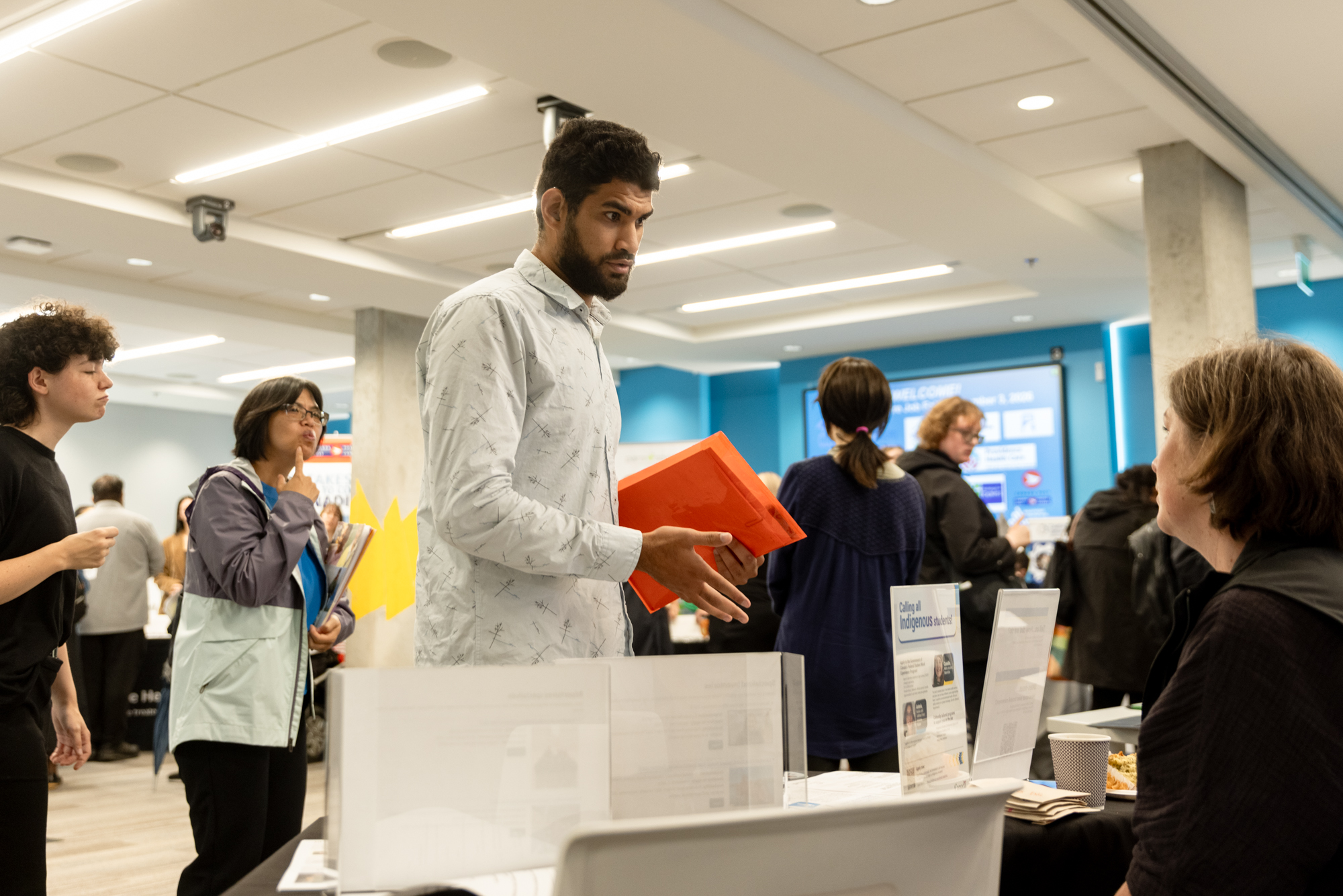 A job seeker holding a red folder speaks with an employer representative at Wavefront Centre’s 2026 Job Fair.