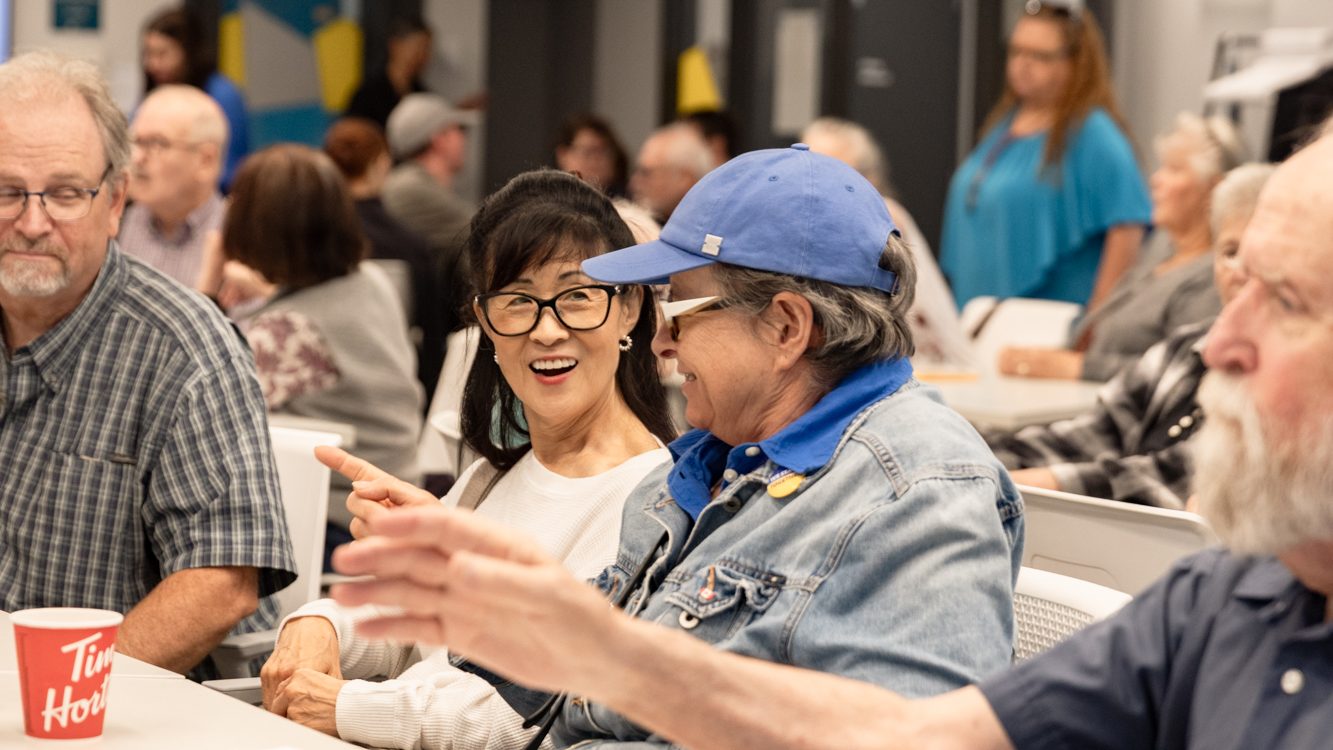 Deaf, DeafBlind and Hard of Hearing seniors socialize around tables during a Social Meals event at Wavefront Centre.